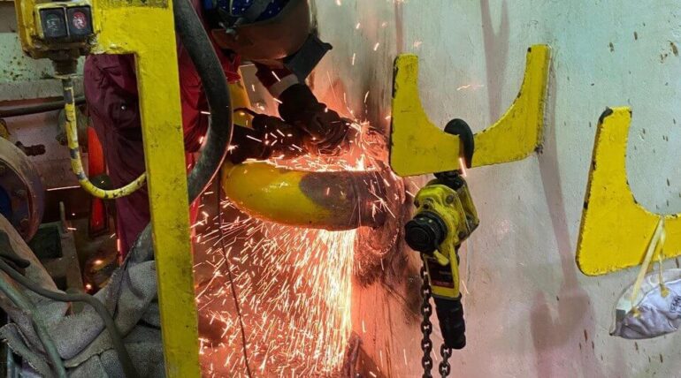 Coded welder grinding a repair inside an offshore vessel compartment