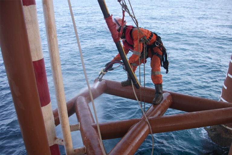 IRATA rope access technician high-pressure jetting an offshore platform jacket member